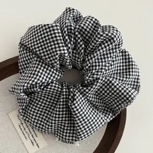 Detail van een zwart-wit geruite scrunchie op een houten dienblad in de zon