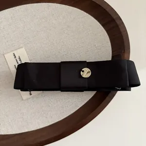 Détail d'une pince à cheveux nœud en satin noir avec emblème en métal doré gravé