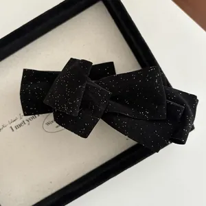 Detailed macro view of black velvet bow hair clip with shimmering gold glitter sparkles