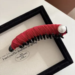 Dettaglio di un fermaglio per capelli in velluto rosso con perla in scatola di legno