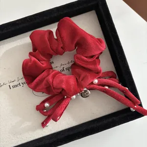 Dettaglio dell'elastico in velluto rosso con perle e targhetta in metallo dorato