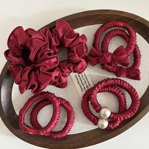 Detail von weinroten Satin-Haargummis und eleganten Haarbändern mit Perlen und Schleifen