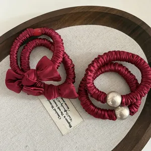 Nahaufnahme roter Satin-Haargummis mit Schleife und Silberperle auf Holztablett