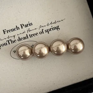 Détail de quatre perles métalliques dorées champagne sur une barrette de style vintage