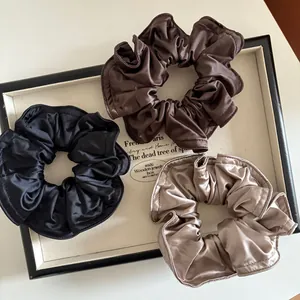 Drei elegante Satin-Haargummis in Schwarz, Schoko und Champagner auf Holzdisplay