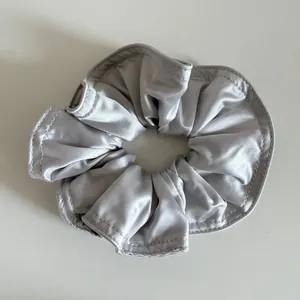 Nahaufnahme eines silbergrauen Satin-Haargummis mit glänzender Seidentextur und Steppnähten