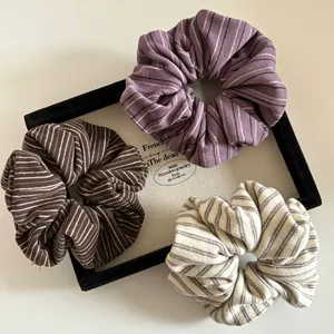 Three-piece striped fabric scrunchies set in purple, brown, and cream on a display tray