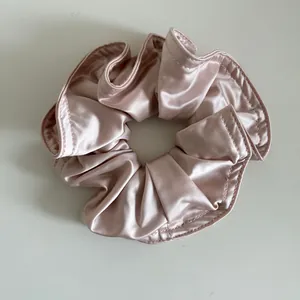 Nahaufnahme vom champagnerrosa Satin-Haargummi mit plissierter Textur und feiner Naht