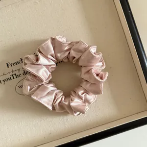 Détail d'un chouchou en satin plissé de haute qualité rose champagne à texture soyeuse