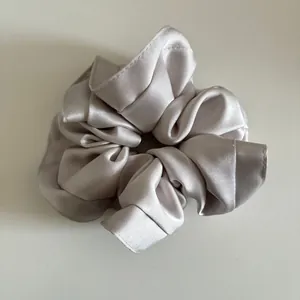 Detail shot of oversized champagne satin scrunchie showing smooth silk texture and soft pleats