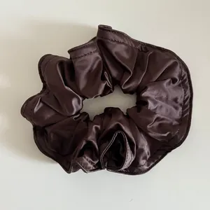Detailansicht des dunkelbraunen Satin-Haargummis mit feiner Naht und plissierter Textur