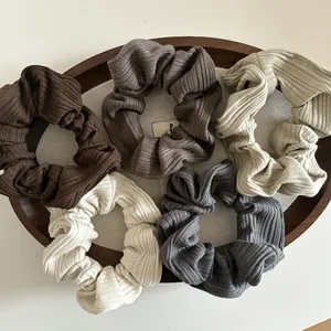 Détail de cinq chouchous en tricot côtelé aux tons neutres posés sur un plateau en bois