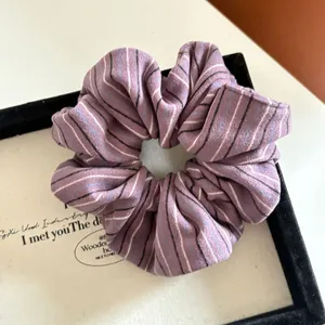 Detailed close-up of a purple striped fabric scrunchie with soft pleated texture and elastic