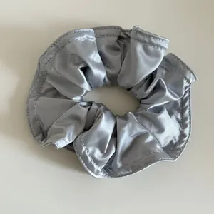 Detailansicht eines silbergrauen Satin-Haargummis mit glatter Textur und präziser Naht