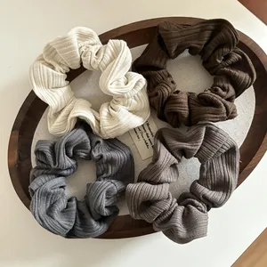 Lot de quatre chouchous en maille côtelée crème, marron et gris sur plateau bois