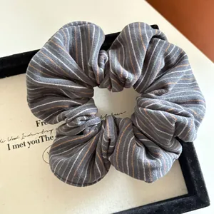 Detail shot of a dark grey striped knitted scrunchie on a minimalist white display