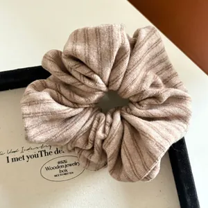 Detail of a beige striped knit scrunchie inside a minimalist wooden jewelry box display