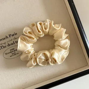 Détail du chouchou en satin doré champagne avec bords plissés dans un coffret cadeau