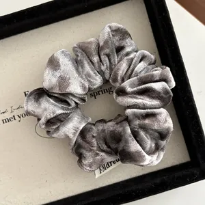 Macro shot of a grey velvet scrunchie with soft sheen and woven brand label on white card