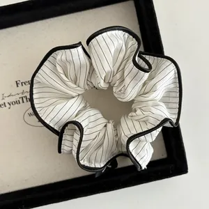 Close-up of a striped fabric scrunchie with black piping and pleated texture on a tray