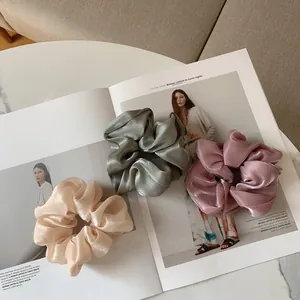 Trois chouchous en satin de haute qualité en beige, vert et rose sur un magazine