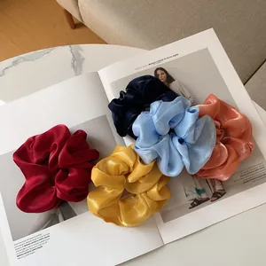 Détail de cinq chouchous en satin brillant disposés sur un magazine de mode chic