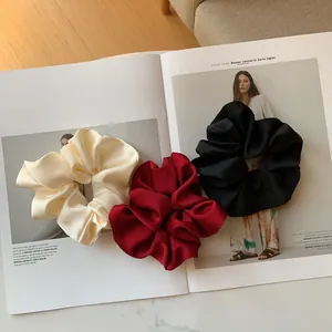 Detailed texture of silk satin scrunchies in cream, wine red, and black colors
