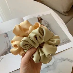Beige and sage green oversized silk satin scrunchies held over a fashion magazine