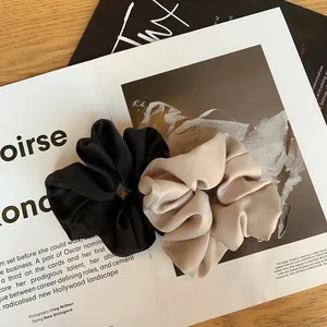 Détails de chouchous en satin noir et beige à texture mate posés sur un magazine de mode