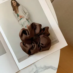 Detail of a large dark brown silk satin scrunchie placed on a fashion magazine