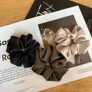 Lot de trois chouchous en satin plissé noir, vert et beige posés sur une table en bois