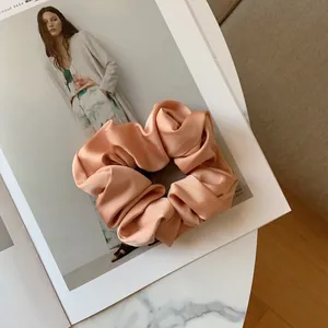 Macro view of silky satin scrunchie with soft peach pleats on a marble surface