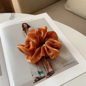 Détails de texture du chouchou en satin orange brillant posé sur un magazine de mode