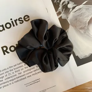 Vue détaillée d'un chouchou en satin noir texturé posé sur un magazine de mode