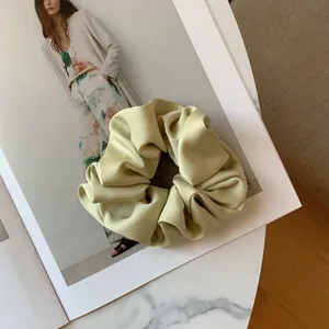 Detailed close-up of a premium sage green pleated satin hair scrunchie on a magazine