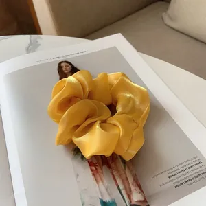 Gros plan d'un chouchou en satin jaune brillant posé sur un magazine de mode chic