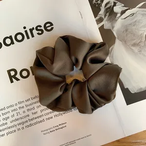 Détail d'un chouchou en soie marron foncé texturé sur un magazine de mode épuré