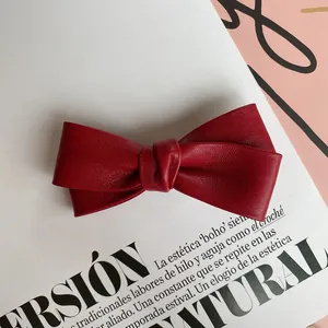 Detail shot of a dark red PU leather bow hair clip with lychee texture on a magazine