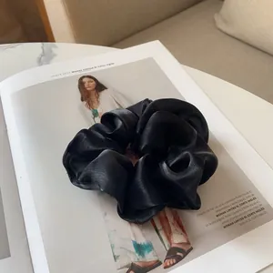 Détail d'un grand chouchou en satin noir plissé posé sur une page de magazine de mode
