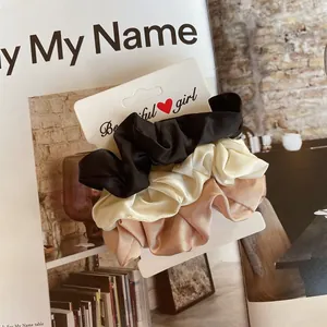 Détail de chouchous en satin de soie noir, crème et champagne posés sur un magazine