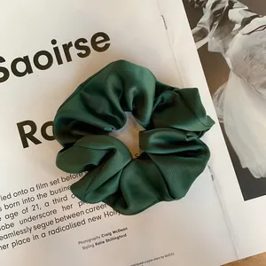 Détail d'un chouchou en satin vert foncé montrant la texture plissée sur un magazine
