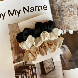 Lot de trois chouchous en satin de soie noir, crème et or champagne sur présentoir