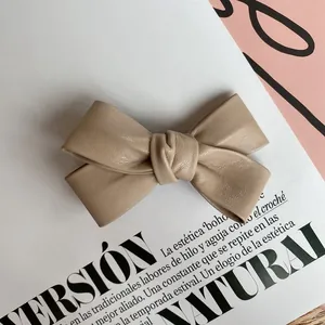 Close-up of beige PU leather bow hair clip with textured finish on a magazine page