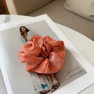 Détail d'un chouchou en satin orange corail avec texture brillante plissée sur magazine