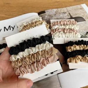 Close-up of four silk satin hair scrunchies in neutral tones on a white display card