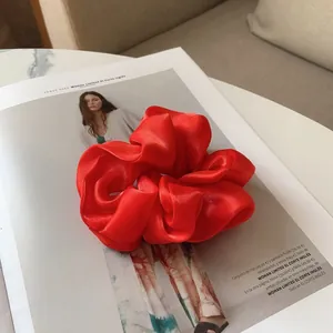 Gros plan sur un grand chouchou en satin rouge plissé sur un fond de magazine de mode de luxe