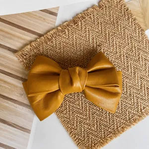 Detailed view of ginger yellow leather bow hair clip on a textured woven mat background