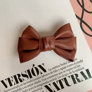 Detailed close-up of dark brown leather bow hair clip with textured retro finish