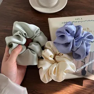 Three elegant satin scrunchies in mint, cream, and lavender on a wooden desk