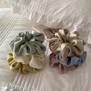 Elegant set of six satin silk scrunchies in various pastel colors on a white bedding